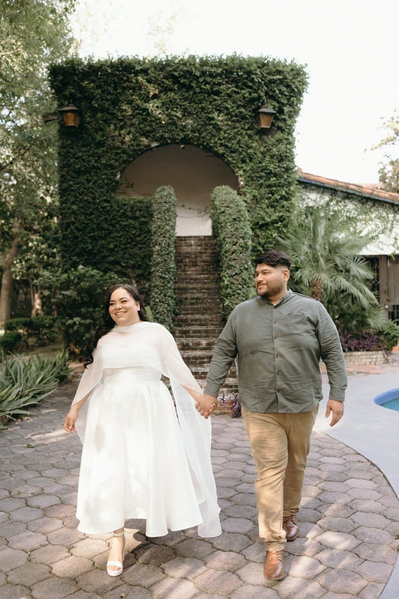 Karla y Christian caminando de la mano frente a una escalera cubierta de hiedra